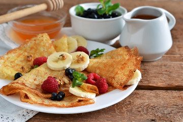 Homemade pancakes with banana, berries and honey for breakfast on a wooden background