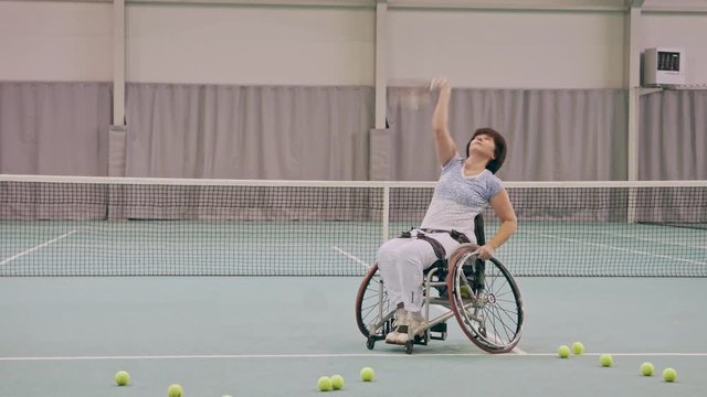 Disabled mature woman on wheelchair playing tennis on tennis court.