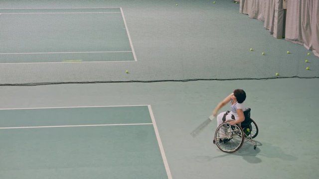 Disabled mature woman on wheelchair playing tennis on tennis court.