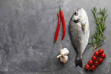 Fresh dorado or gilthead bream cooking with rosemary, cherry tomatoes, chili pepper and garlic on stone background