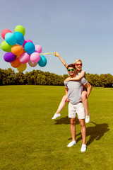 Young couple having fun on weekend and walking with balloons. Man piggybacking his girlfriends