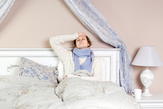 Flu or cold. Closeup top view image of frustrated young woman with blue scarf and suffering from terrible headache while lying in bed.