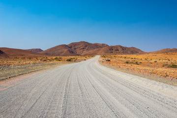 Gravel 4x4 road crossing the colorful desert at Twyfelfontein, in the majestic Damaraland Brandberg, scenic travel destination in Namibia, Africa.