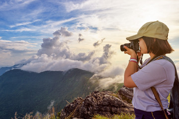 Hiker asian teens girl with digital camera and backpack taking photo beautiful landscape natural of sierra and sky during sunset on mountain at Phu Chi Fa Forest Park, Chiang Rai, Thailand
