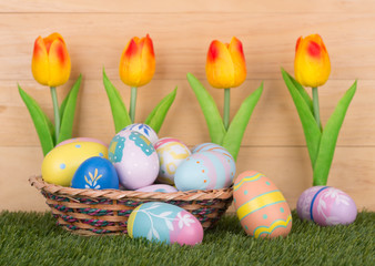 Fototapeta na wymiar Colorful Easter Eggs and Tulips Against a Wooden Background