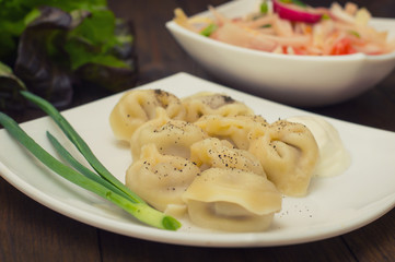 Russian pelmeni with fresh green onion on plate. Wooden background. Top view. Close-up