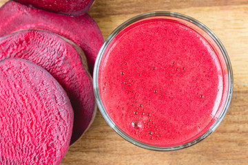 Fresh beet juice in glass and sliced beetroot on wooden table, top view.