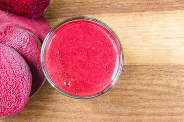 Fresh beet juice in glass and sliced beetroot on wooden table, top view.