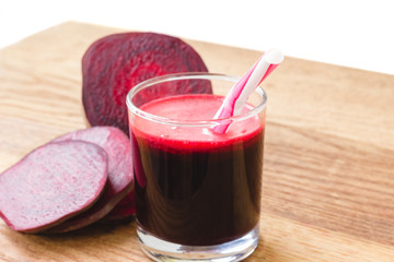 Fresh beet juice in glass and sliced beetroot on wooden table, white background.