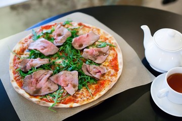 Pizza with roast beef and rocket salad on a table