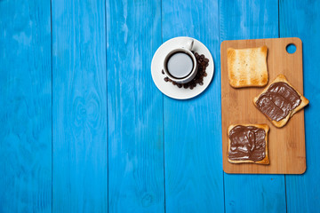 Cup of coffee and toast with chocolate on a blue wooden table