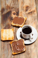 cup with coffee, toast and chocolate on wooden table