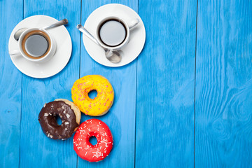 Obraz na płótnie Canvas Two cups with coffee and donuts on a blue wooden table
