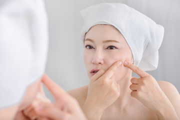 woman squeezing pimple in front of mirror