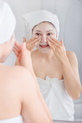 woman applying mask on her face and looking in the mirror