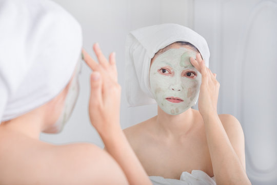 woman applying mask on her face and looking in the mirror