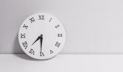 Closeup white clock for decorate show half past seven or 7:30 a.m. on white wood desk and wallpaper textured background in black and white tone with copy space