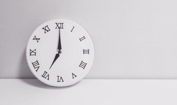 Closeup white clock for decorate in 7 o'clock on white wood desk and wallpaper textured background in black and white tone with copy space