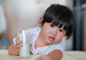 Close up of little girl in pajamas drinking milk from glass indoor at the morning.