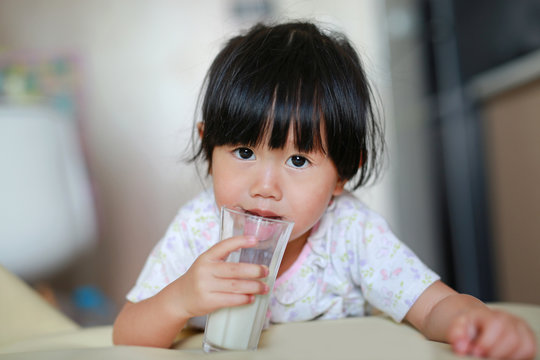 Close up of little girl in pajamas drinking milk from glass indoor at the morning.
