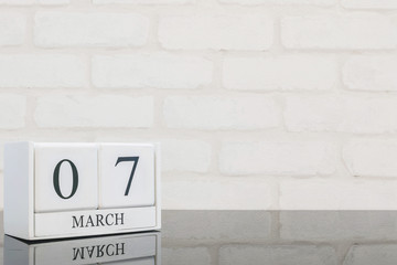 Closeup white wooden calendar with black 7 march word on black glass table and white brick wall textured background with copy space , selective focus at the calendar