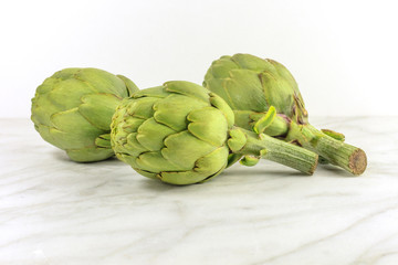 Fototapeta premium Artichokes on white marble texture with copyspace