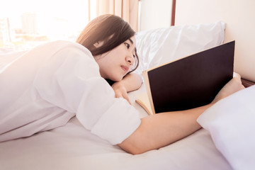 Woman reading book  and drinking coffee on bed during the morning