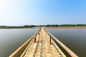 Fototapeta na wymiar beautiful long bamboo bridge on river with blue sky at sunny day. soft focus
