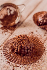 Chocolate chip muffin in brown wax paper. Unwrapped. Cocoa powder in the background