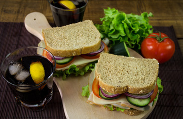 Sandwich with ham, cheese, tomatoes, lettuce, cucumbers and onions on a wooden background