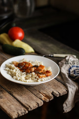 Fish in tomato sauce and pasta in a white plate on a wooden surface (on a table) and vegetables