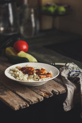 Fish in tomato sauce and pasta in a white plate on a wooden surface (on a table) and vegetables
