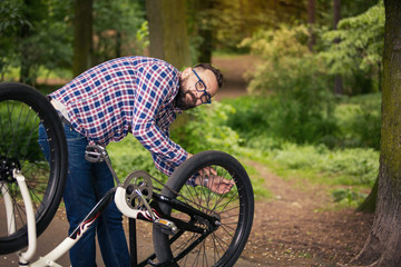 Young trendy man repairing bike wheel in park