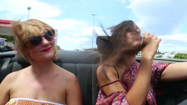 Two beautiful young female friends having fun riding in convertible