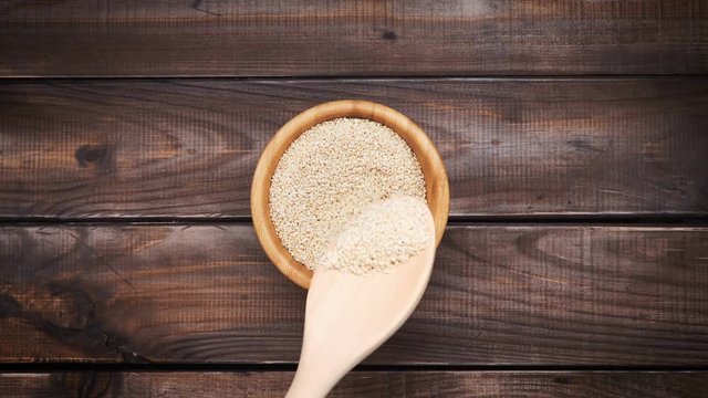 In a wooden bowl, stir sesame with a spoon made of wood. Fashionable background from a tree. Sesame eastern spice or seasoning. Healthy lifestyle
