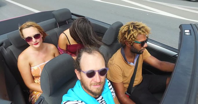 Four young friends having fun riding in convertible