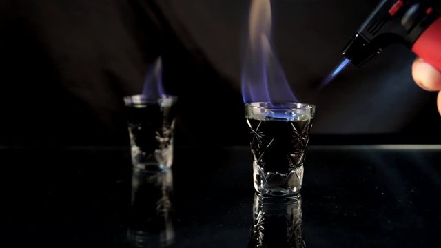 Barman sets fire black absinthe with a lighter. Alcohol of ninety degrees. Fire in the shot.
