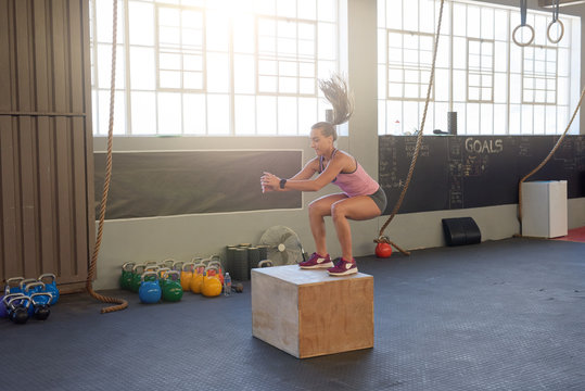 woman box jumps training exercising alone in bright gym