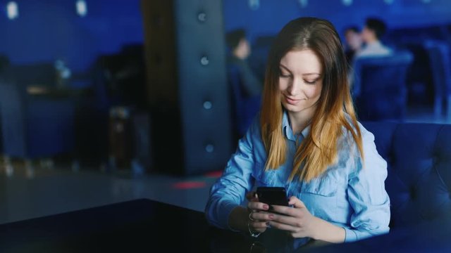 A young woman sits alone in a cafe or nightclub, uses a telephone
