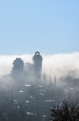 Fog over the city. City is covered with mist in sunlight and blu