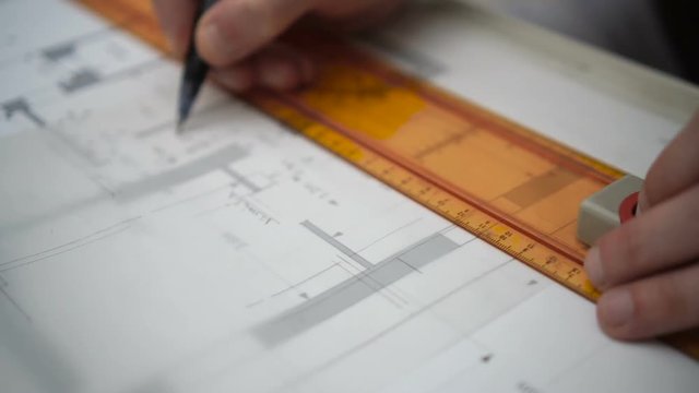 Architect drawing blueprints plan, graph, design, geometric shapes by pencil on large sheet of Tracing paper at office desk. Engineer hands, Working with triangle ruler and pencil