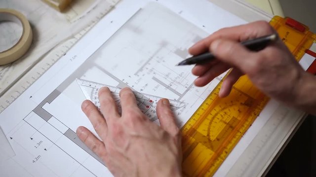 Architect drawing blueprints plan, graph, design, geometric shapes by pencil on large sheet of Tracing paper at office desk. Engineer hands, point of view POV Working with triangle ruler and pencil