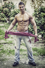 Handsome, athletic man playing with shirt, wearing jeans and showing muscular torso, abs, pecs and...