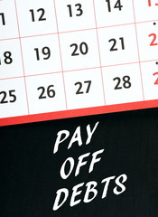 The words Pay Off Debts in white text on a blackboard with a calendar as a reminder of the date