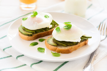 Vegetarian breakfast: avocado toast with poached eggs, orange juice, yogurt and jam on white wooden background. Selective focus