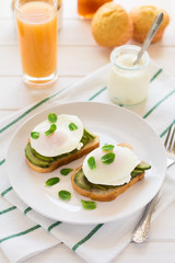 Vegetarian breakfast: avocado toast with poached eggs, orange juice, yogurt and jam on white wooden background. Selective focus