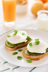 Vegetarian breakfast: avocado toast with poached eggs, orange juice, yogurt and jam on white wooden background. Selective focus