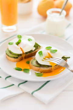 Vegetarian breakfast: avocado toast with poached eggs, orange juice, yogurt and jam on white wooden background. Selective focus