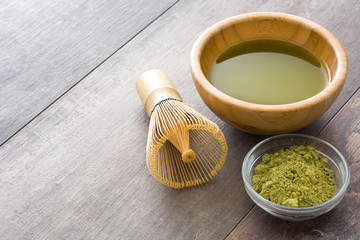 Matcha green tea in a bowl and bamboo whisk, on wooden background
