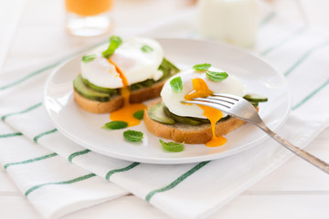 Vegetarian breakfast: avocado toast with poached eggs, orange juice, yogurt and jam on white wooden background. Selective focus